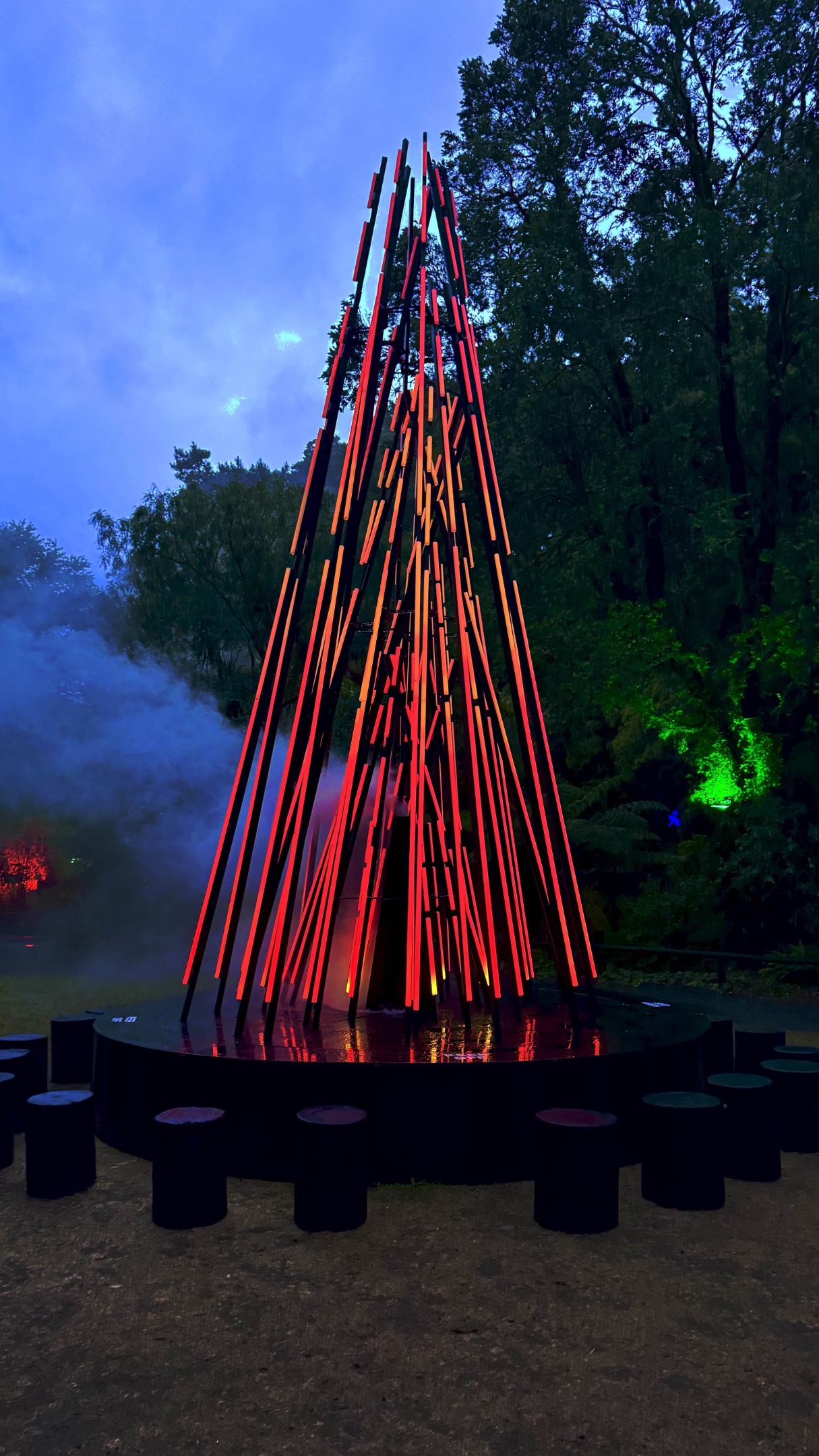The Ember installation in Pukekura Park, with light-filled tubes arranged to resemble a camp fire. Smoke emanates from between the lights as they pulsate between off and glowing red to resemble burning wood.